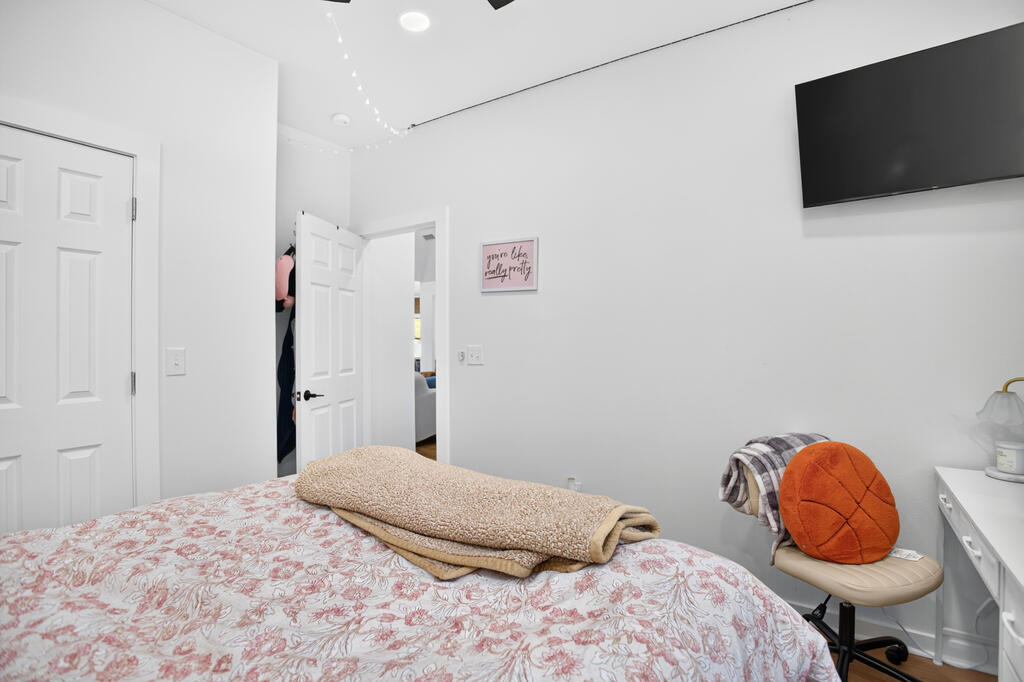 Bedroom with a pink floral bedspread, folded blankets, and a wall-mounted television.