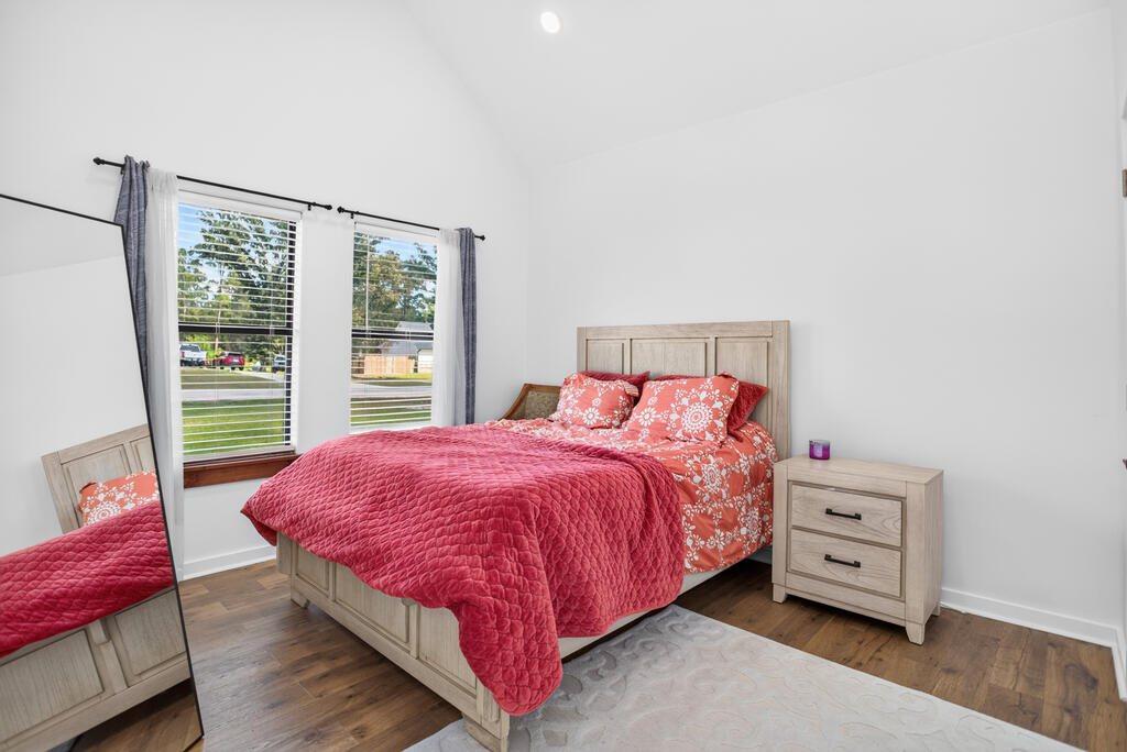 Bedroom with a red quilt, floral bedding, light wood furniture, and two windows.