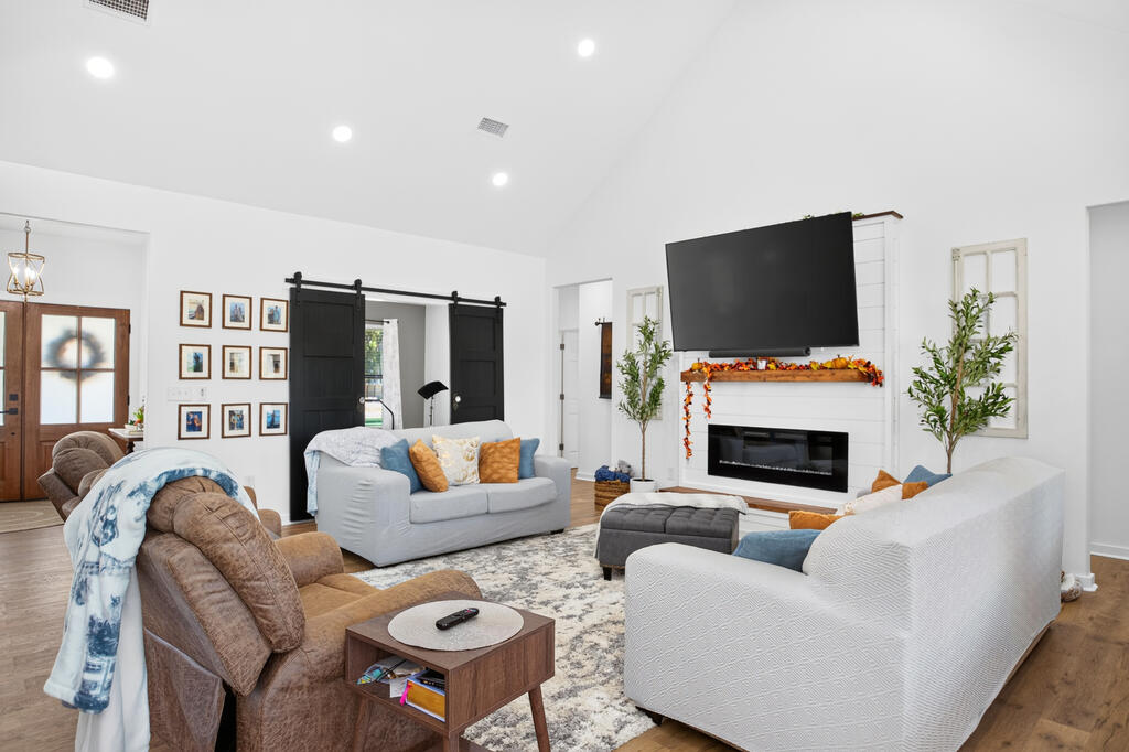 Living room with sofas, a fireplace, and a large television above autumn-decorated mantel
