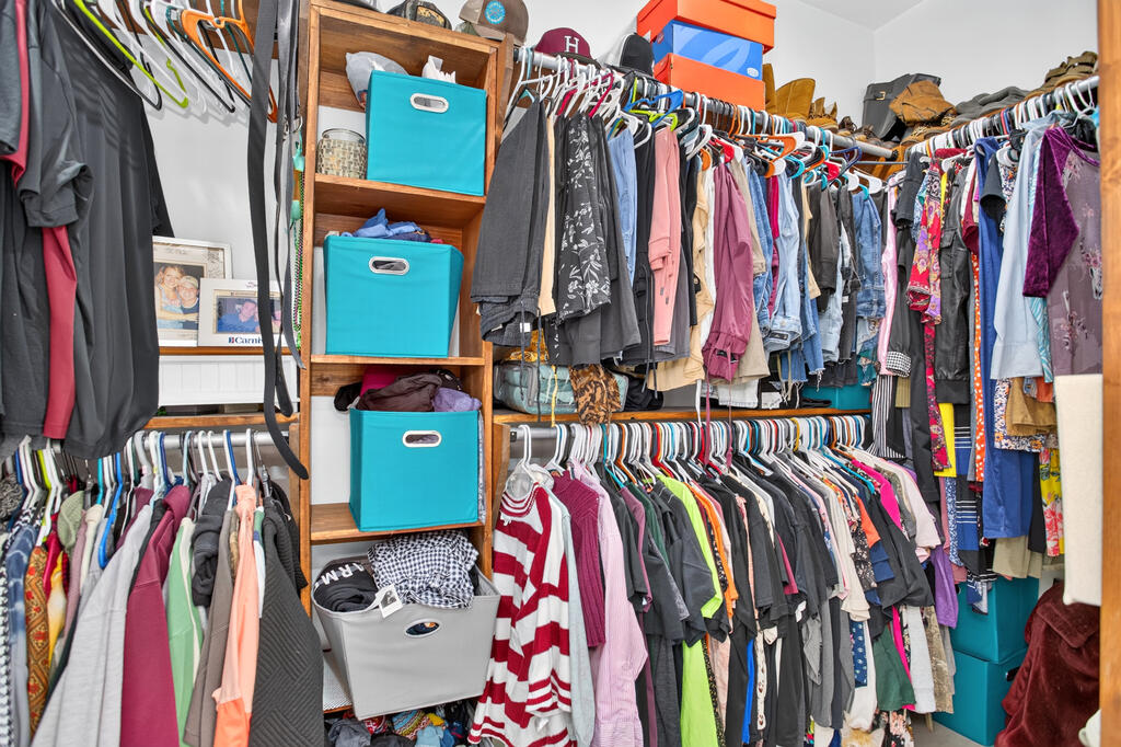 Walk-in closet packed with clothes on two hanging rails and turquoise storage bins on a wooden shelf.