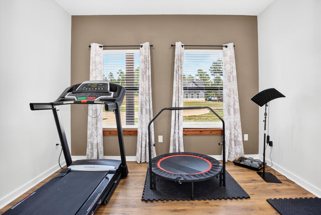 Home gym with a treadmill and mini trampoline between two curtained windows.