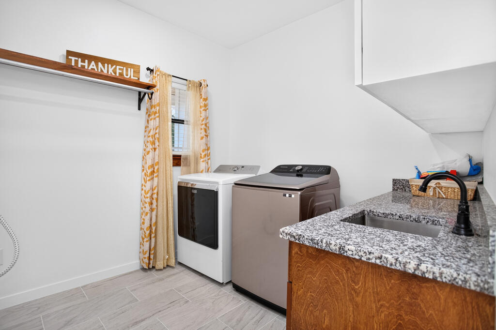 Laundry room with washer and dryer beside a granite sink counter and a window with patterned curtains.