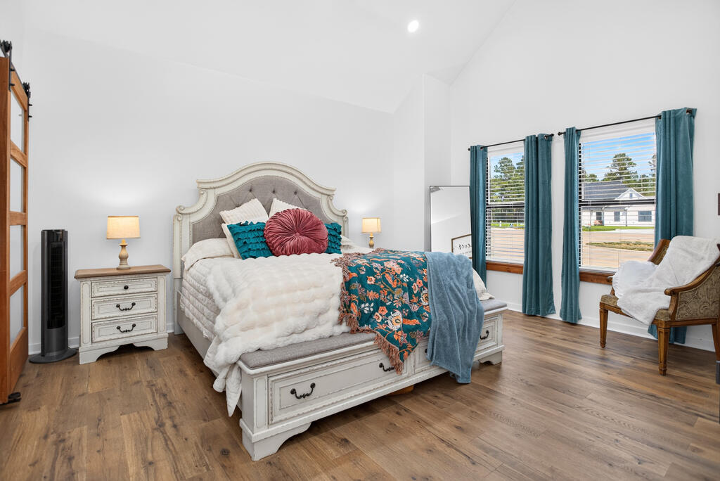 Bedroom with an ornate white bed, teal accents, wood flooring, and two large windows.