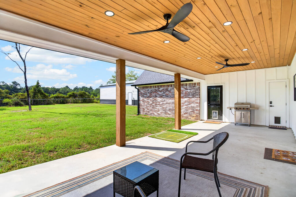 Covered patio with a wood ceiling, ceiling fans, outdoor seating, and a view of the grassy yard.