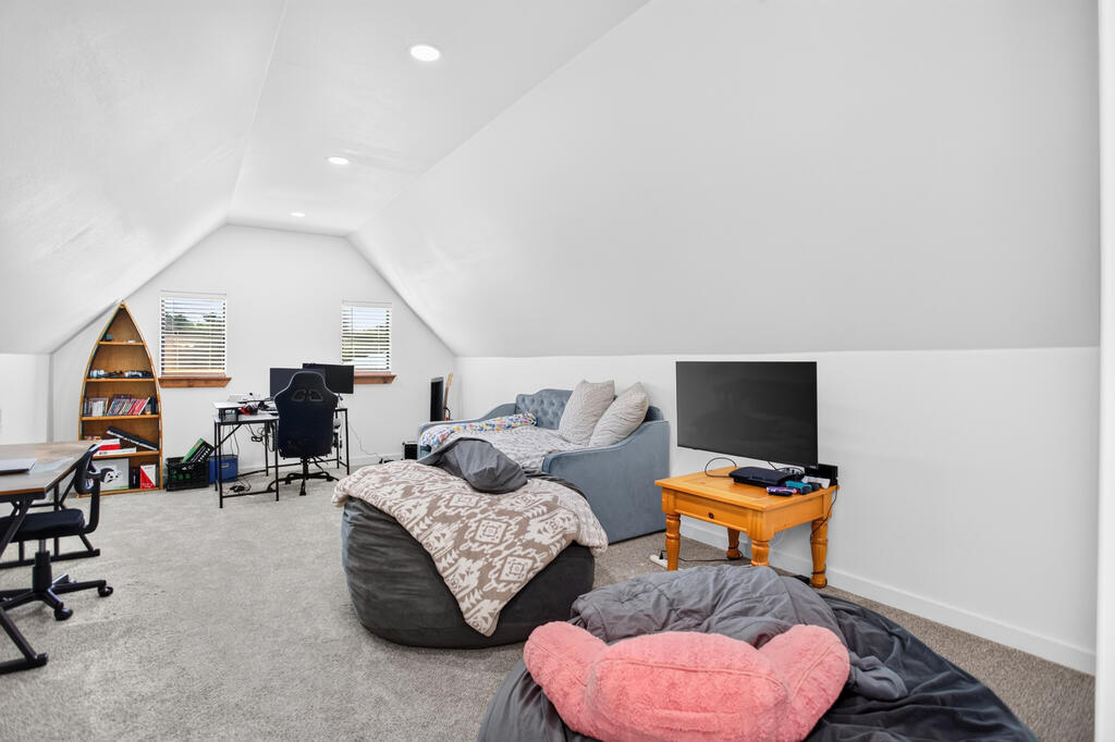 Furnished bonus room with sloped ceiling, blue sofa, television, and desk area.