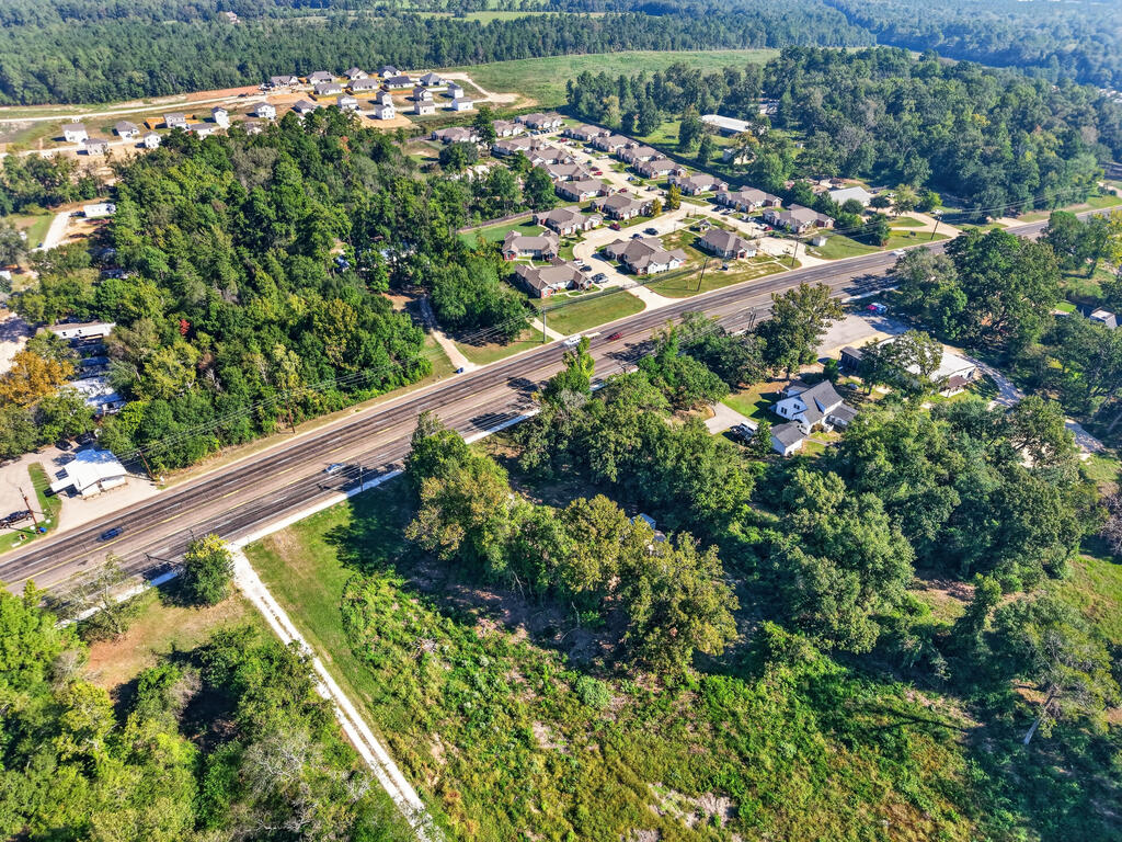 Aerial view of wooded land beside a multi-lane road and residential neighborhood.