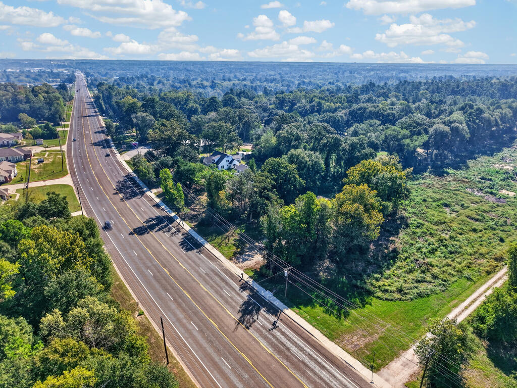 Aerial view of a wooded tract beside a wide road, with open ground and nearby homes.