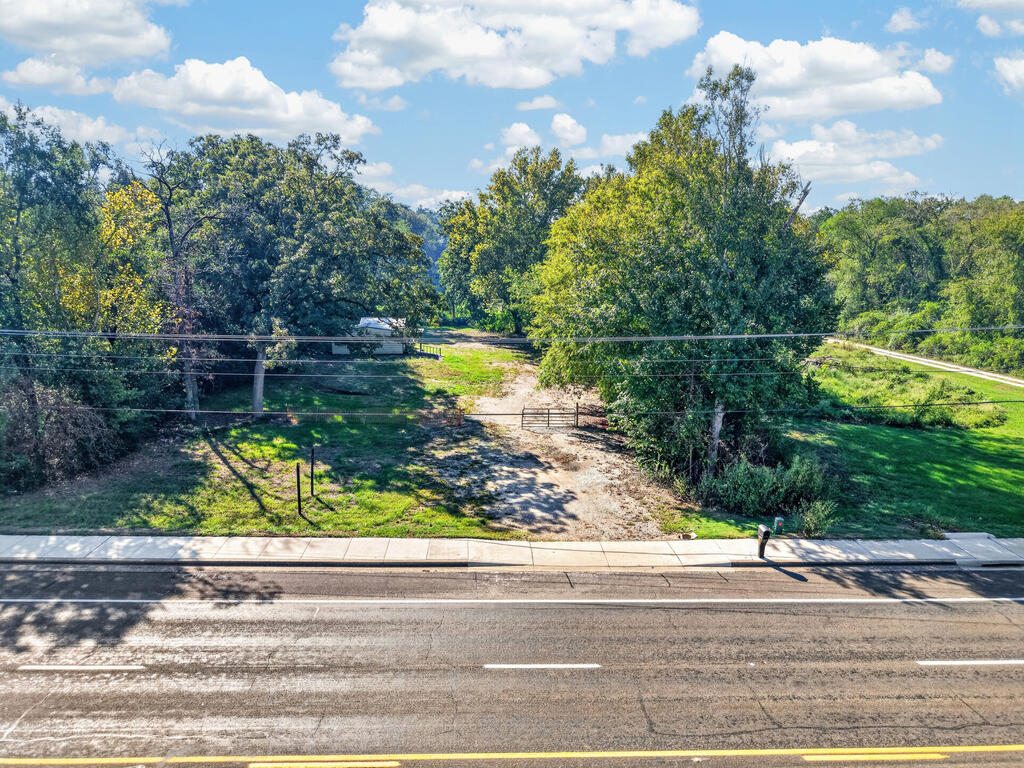 Wooded vacant property with a gated dirt driveway opening onto the road.