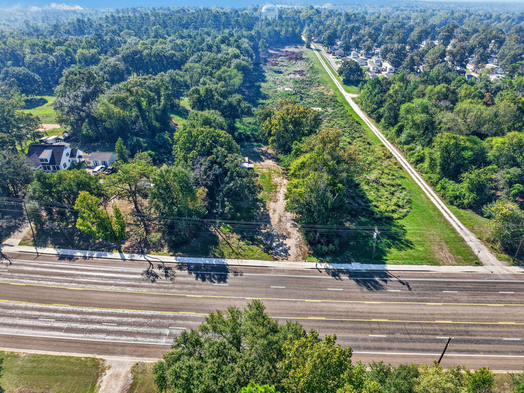 Aerial view of a wooded vacant tract with road frontage and nearby homes.