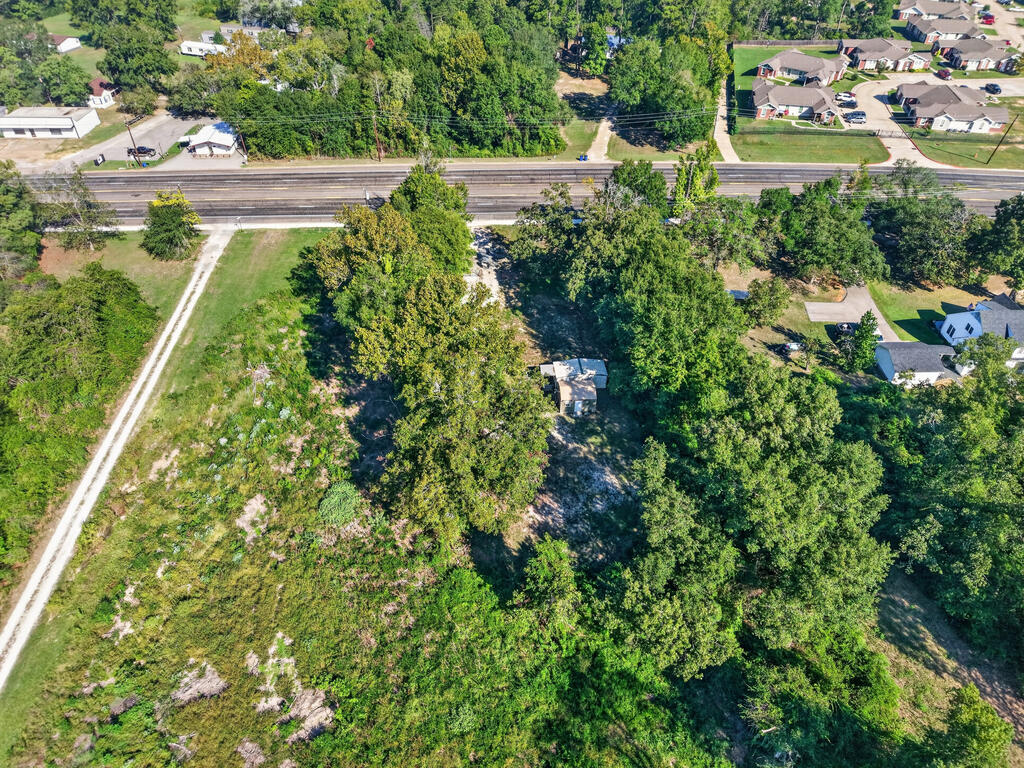 Aerial view of a wooded property with a small structure beside a road.