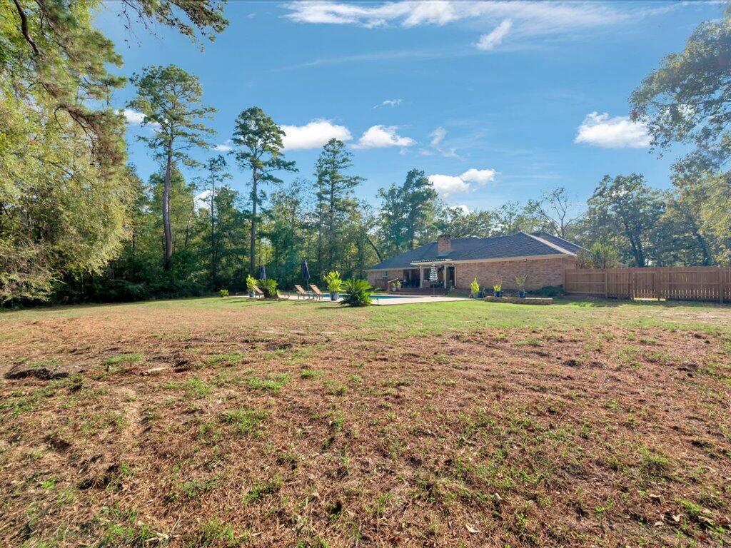 Spacious backyard with mature trees, a swimming pool, patio seating, and a brick house.