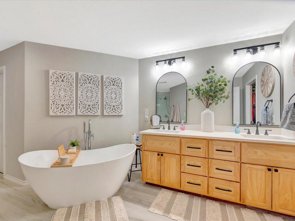 Bathroom with a freestanding soaking tub and light-wood double vanity beneath arched mirrors.