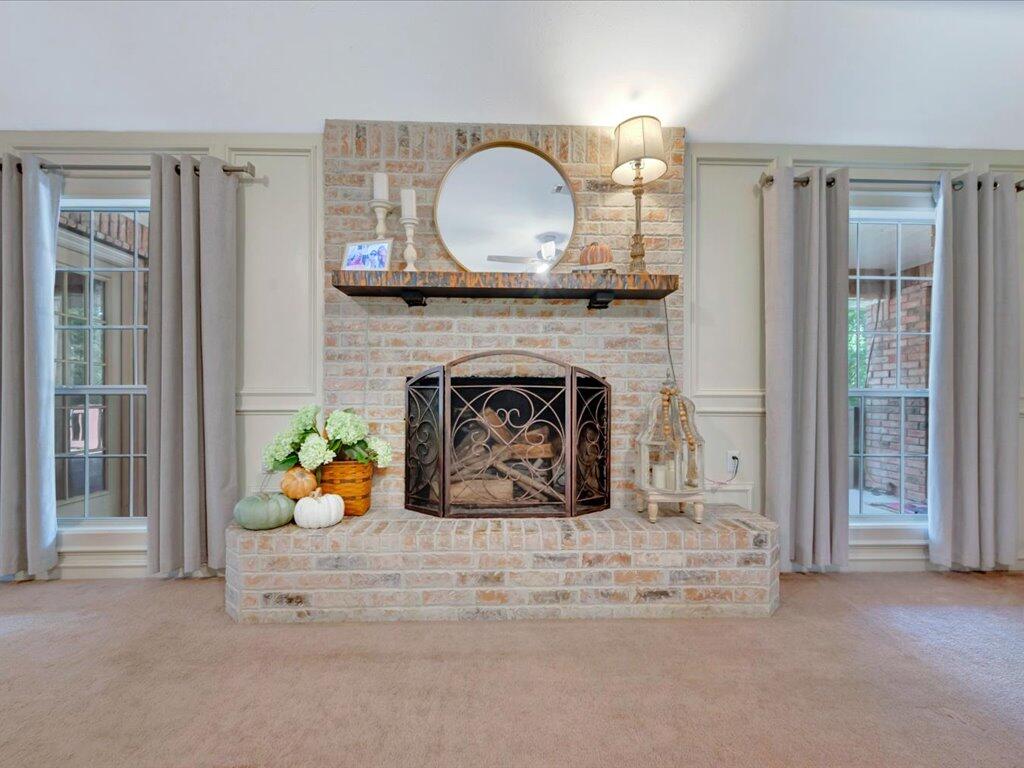 Living room with a raised brick fireplace, round mirror, and curtained windows on either side.