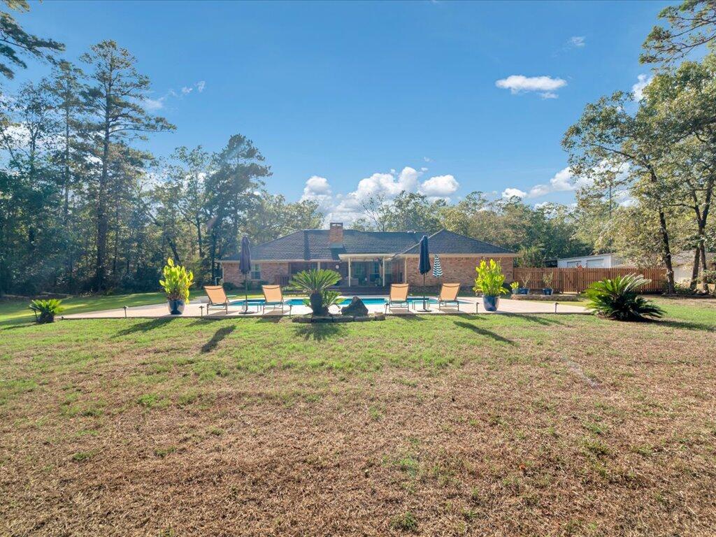 Brick home with a swimming pool and patio seating overlooking a spacious lawn.