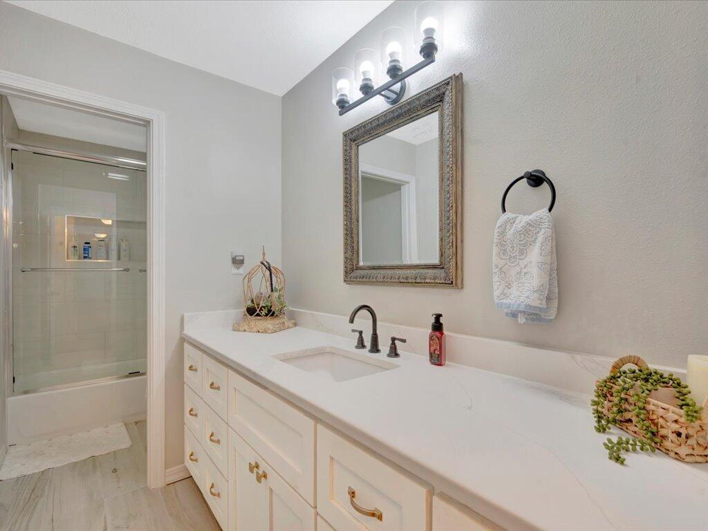 Bathroom with a long white vanity, ornate framed mirror, and glass-enclosed tub and shower.