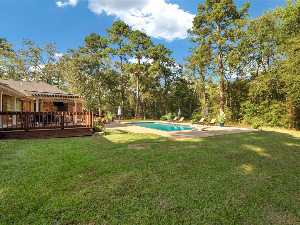 Backyard pool beside a wooden deck, with lounge chairs, lawn, and mature trees.
