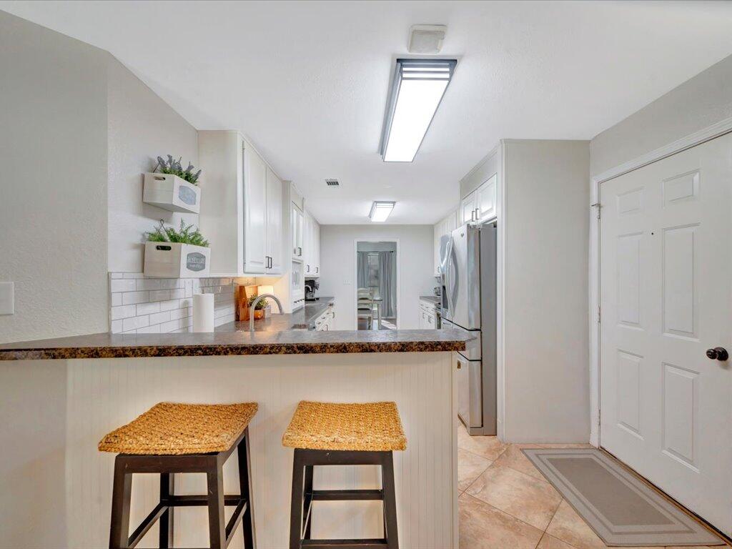 Compact kitchen with white cabinets, stainless appliances, and a breakfast bar with two woven-seat stools.