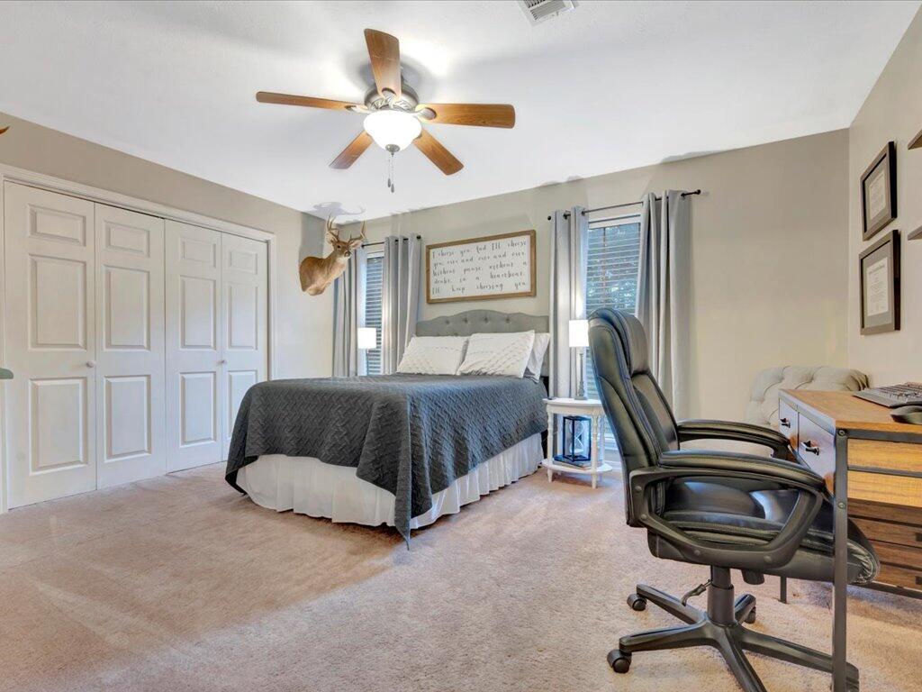 Bedroom with a gray-covered bed, paneled closet doors, mounted deer head, and office chair.