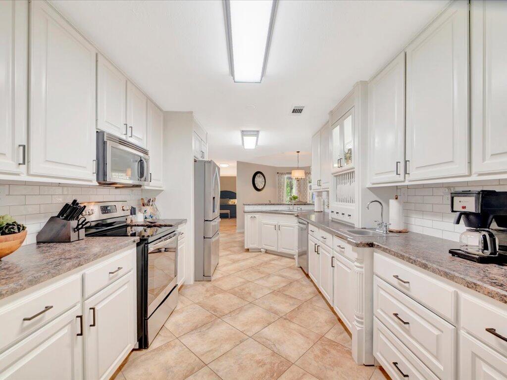 Kitchen with white cabinets, granite counters, stainless steel appliances, and tan tile floors.