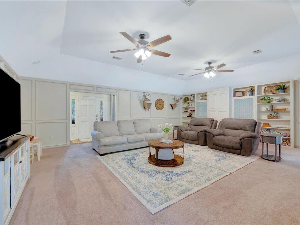 Living room with built-in shelves, two ceiling fans, and a patterned area rug.
