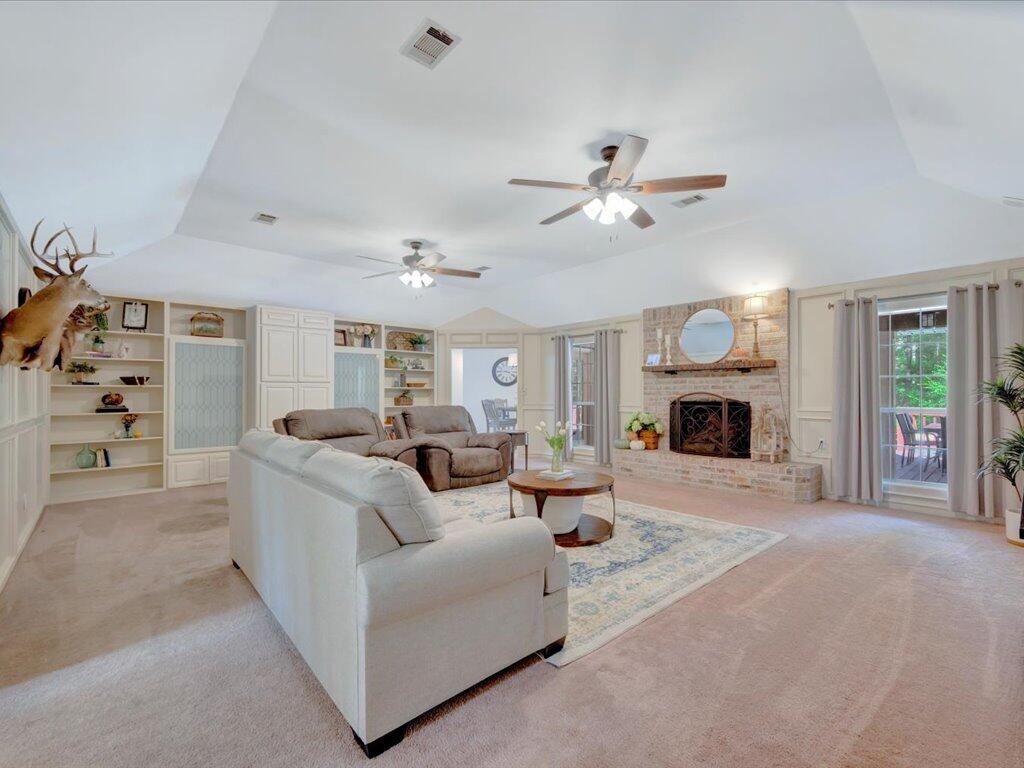 Furnished living room with vaulted ceiling, built-in shelving, brick fireplace, and sliding glass doors.