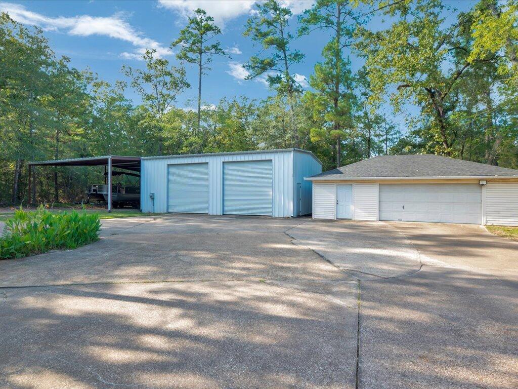 Metal workshop with two roll-up doors beside a white garage and broad paved driveway.