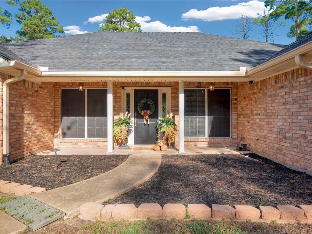 Brick home front with a covered porch, black wreath-adorned door, and curved walkway.