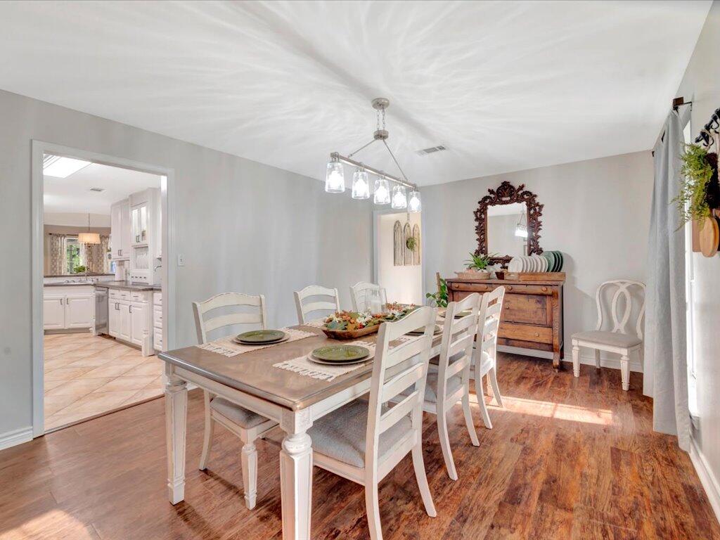 Furnished dining room with a wooden table, white chairs, glass chandelier, and doorway to the kitchen.
