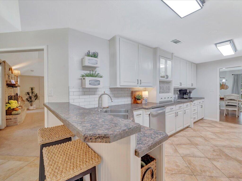 Kitchen with a gray stone island, woven stools, white cabinetry, and stainless steel appliances.