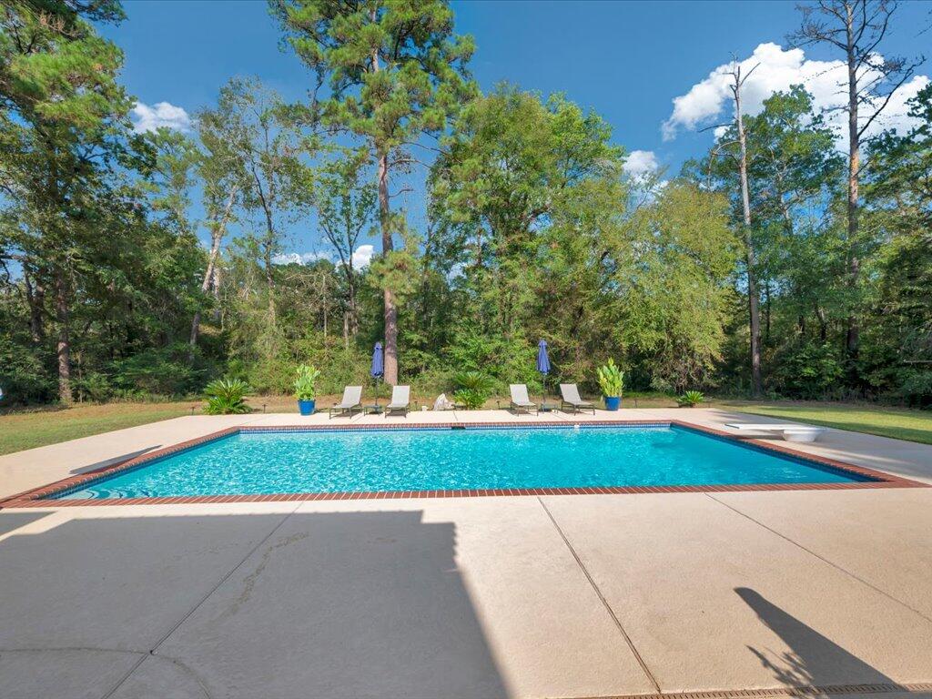 Backyard swimming pool with a wide concrete patio and wooded surroundings.