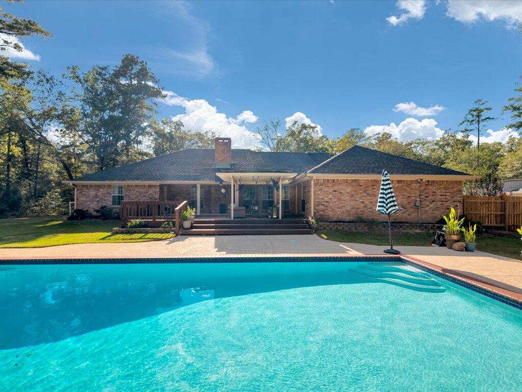 Brick home with a covered patio and deck behind a large swimming pool.