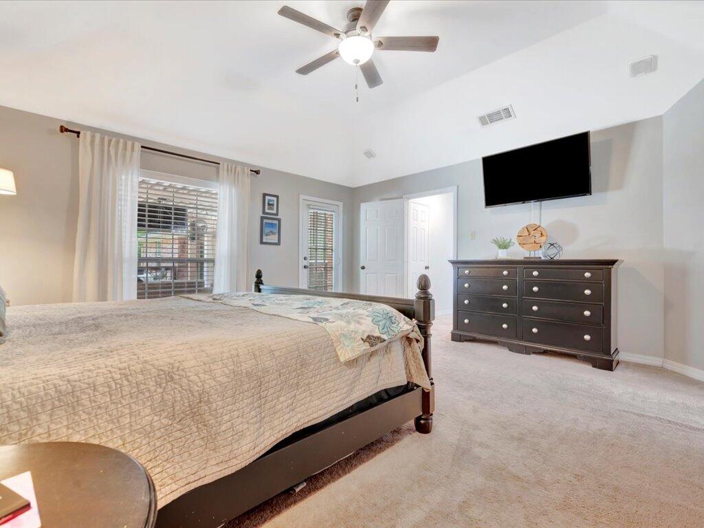 Bedroom with a large bed, dark dresser, wall-mounted television, and ceiling fan.
