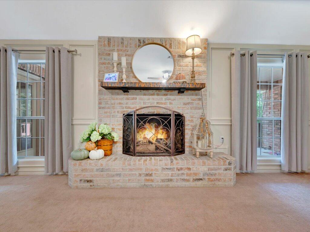 Living room fireplace with a round mirror, brick hearth, and curtained windows.