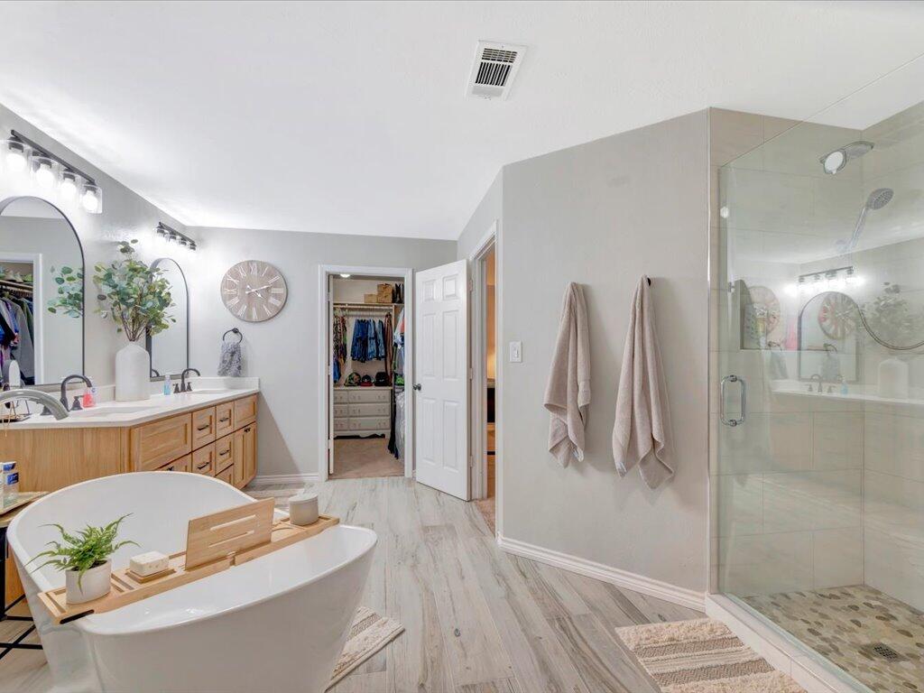 Primary bathroom with a freestanding soaking tub, wood double vanity, and glass-enclosed shower.