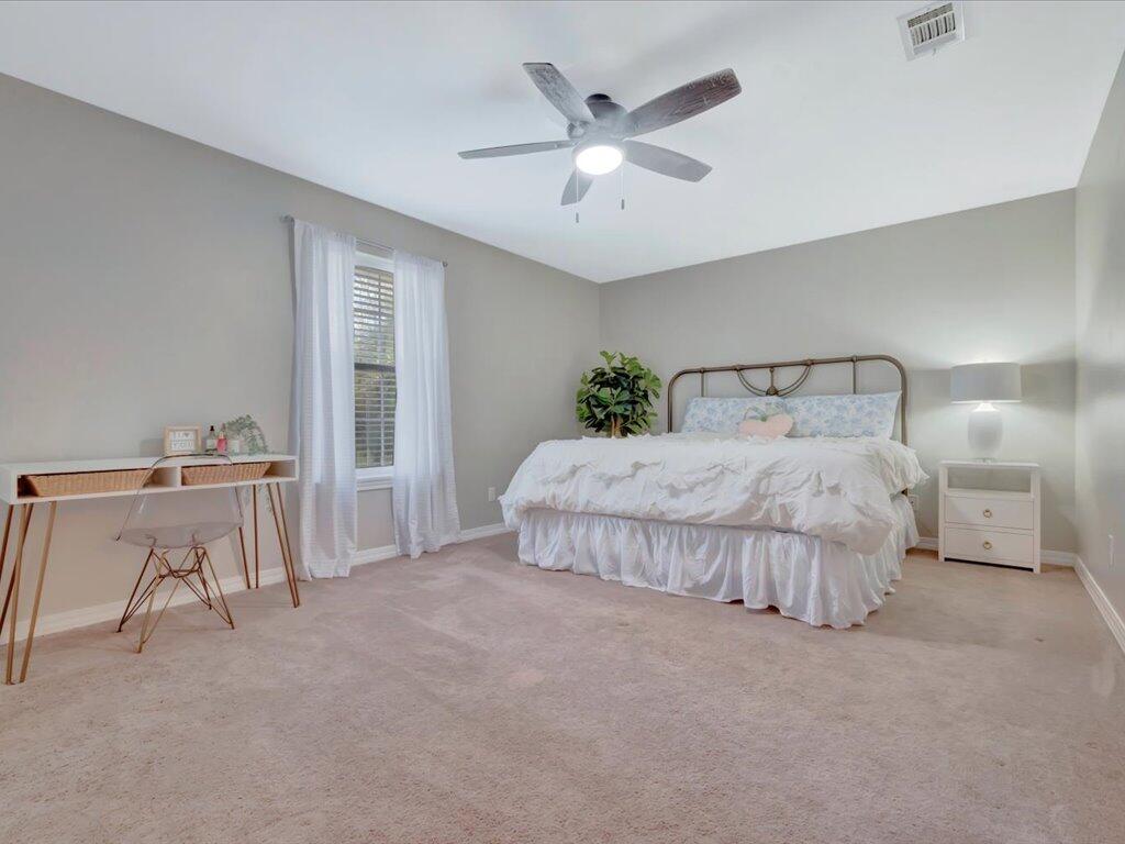 Bedroom with a large bed, curtained window, ceiling fan, and desk.