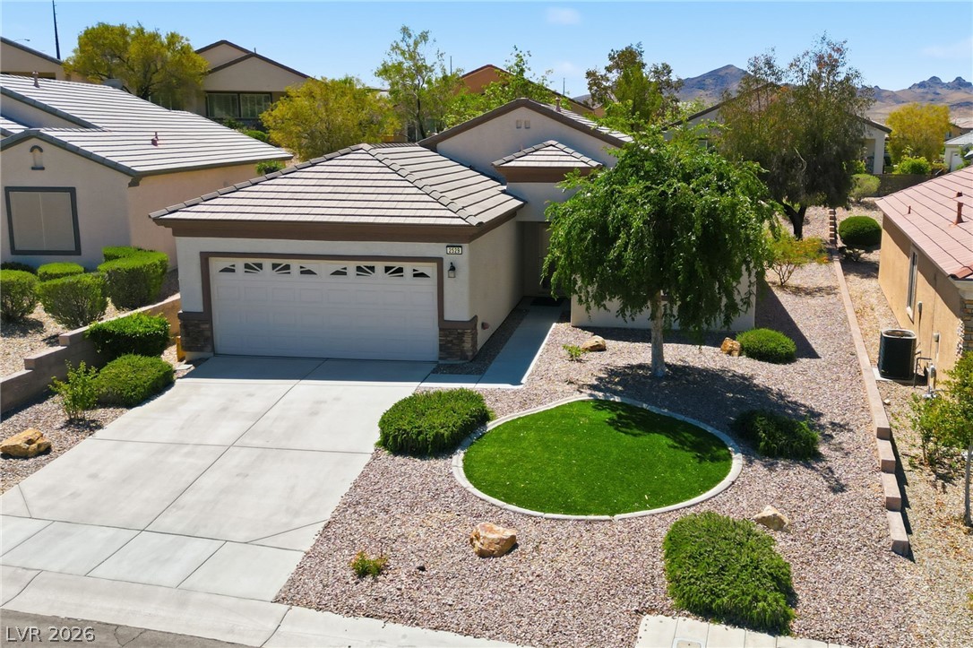 Single-story stucco home with a tile roof, two-car garage, and circular lawn in a gravel yard.