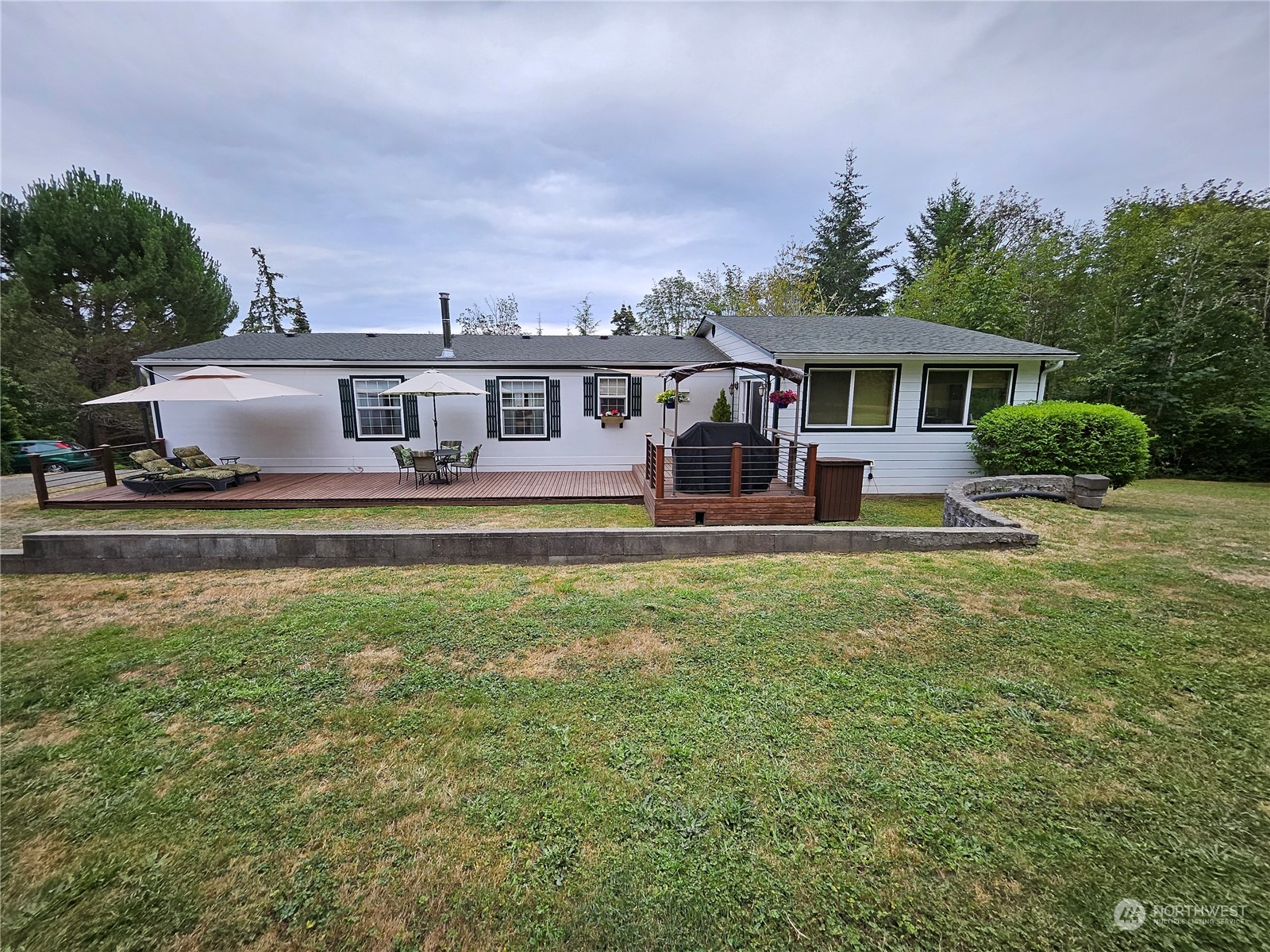 Single-story white home with a long furnished deck, patio umbrellas, and a low retaining wall.