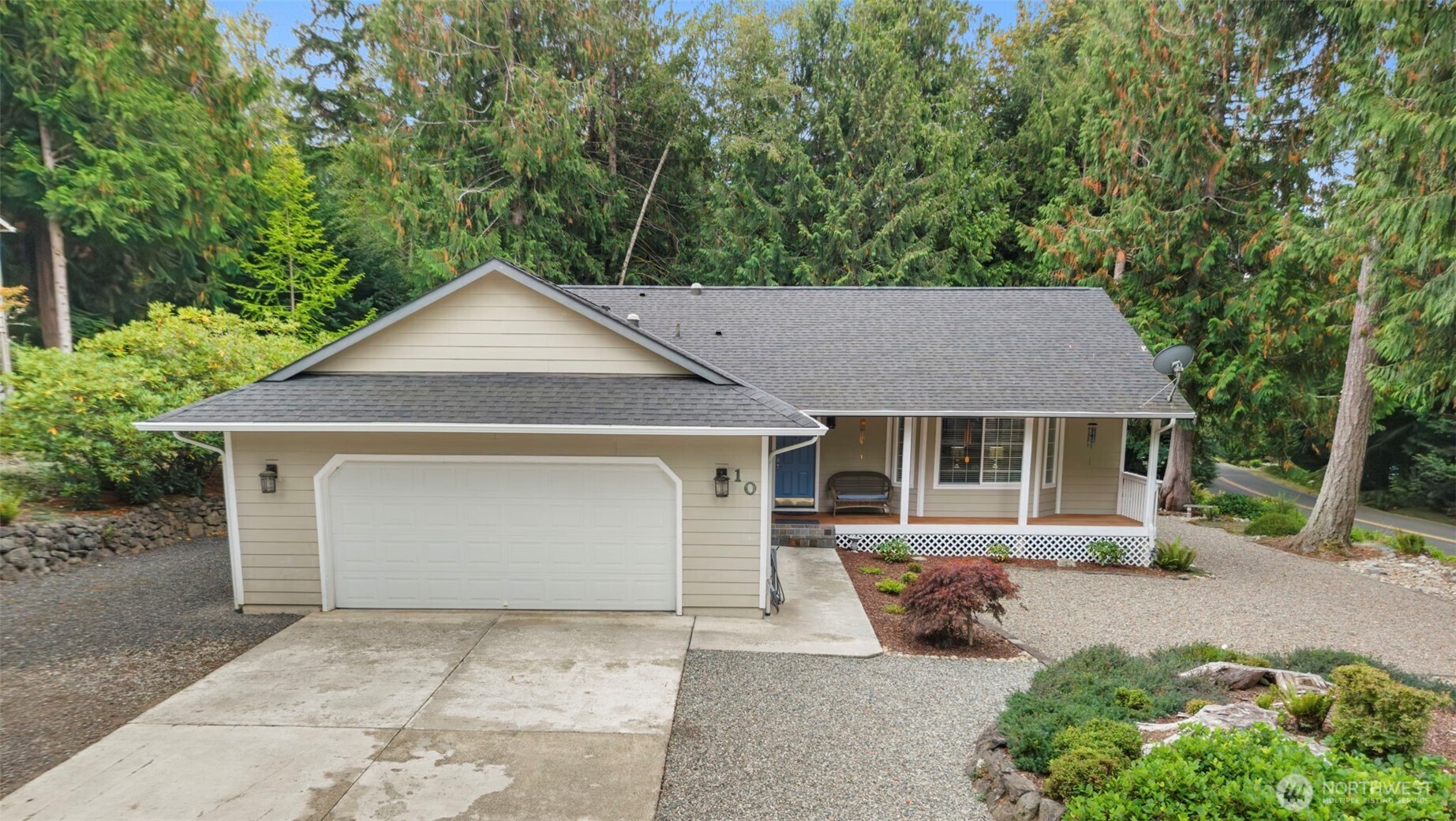 Beige single-story home with a two-car garage and covered porch, surrounded by trees.