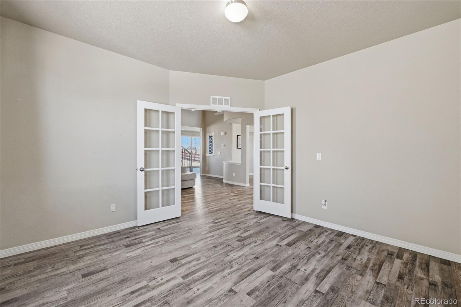 Empty room with gray plank flooring and open French doors to the living area.
