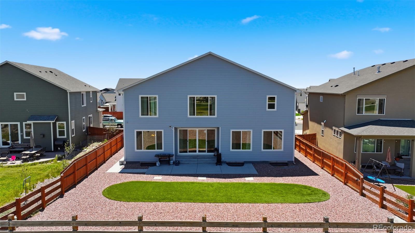 Blue two-story home with a fenced gravel backyard, oval lawn, and rear patio.