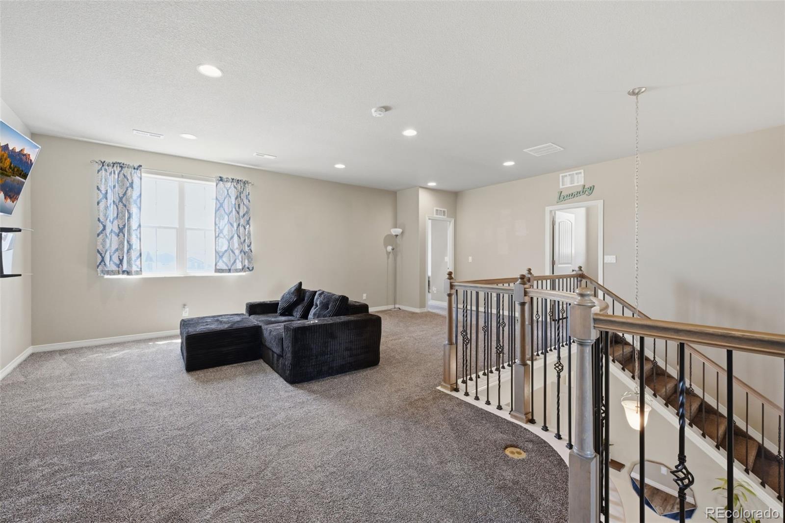 Upstairs loft with a dark sectional, patterned curtains, and a railing overlooking the staircase.