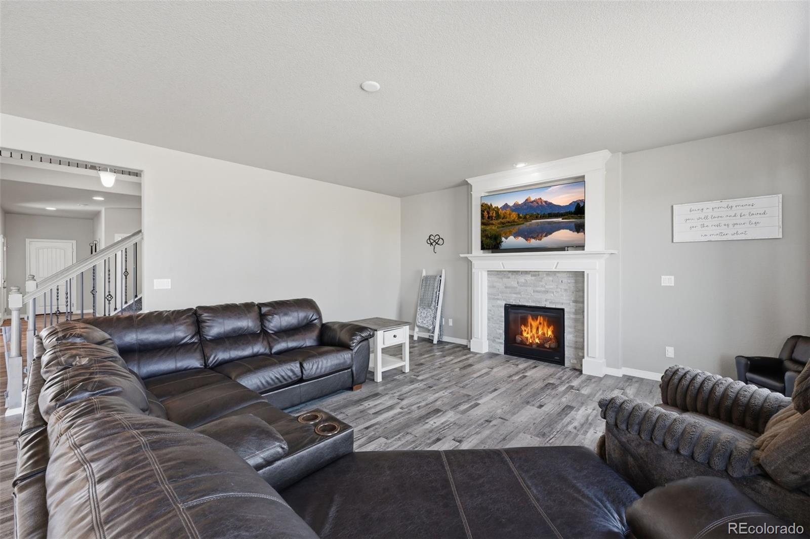 Living room with a leather sectional, gray flooring, and a stone fireplace with a lit fire.