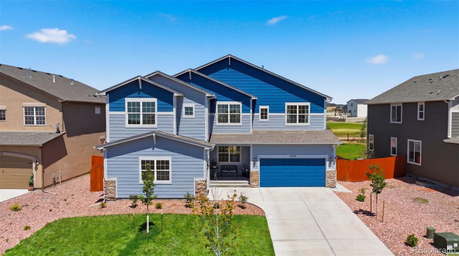 Blue two-story house with a matching garage door, driveway, and landscaped front yard.