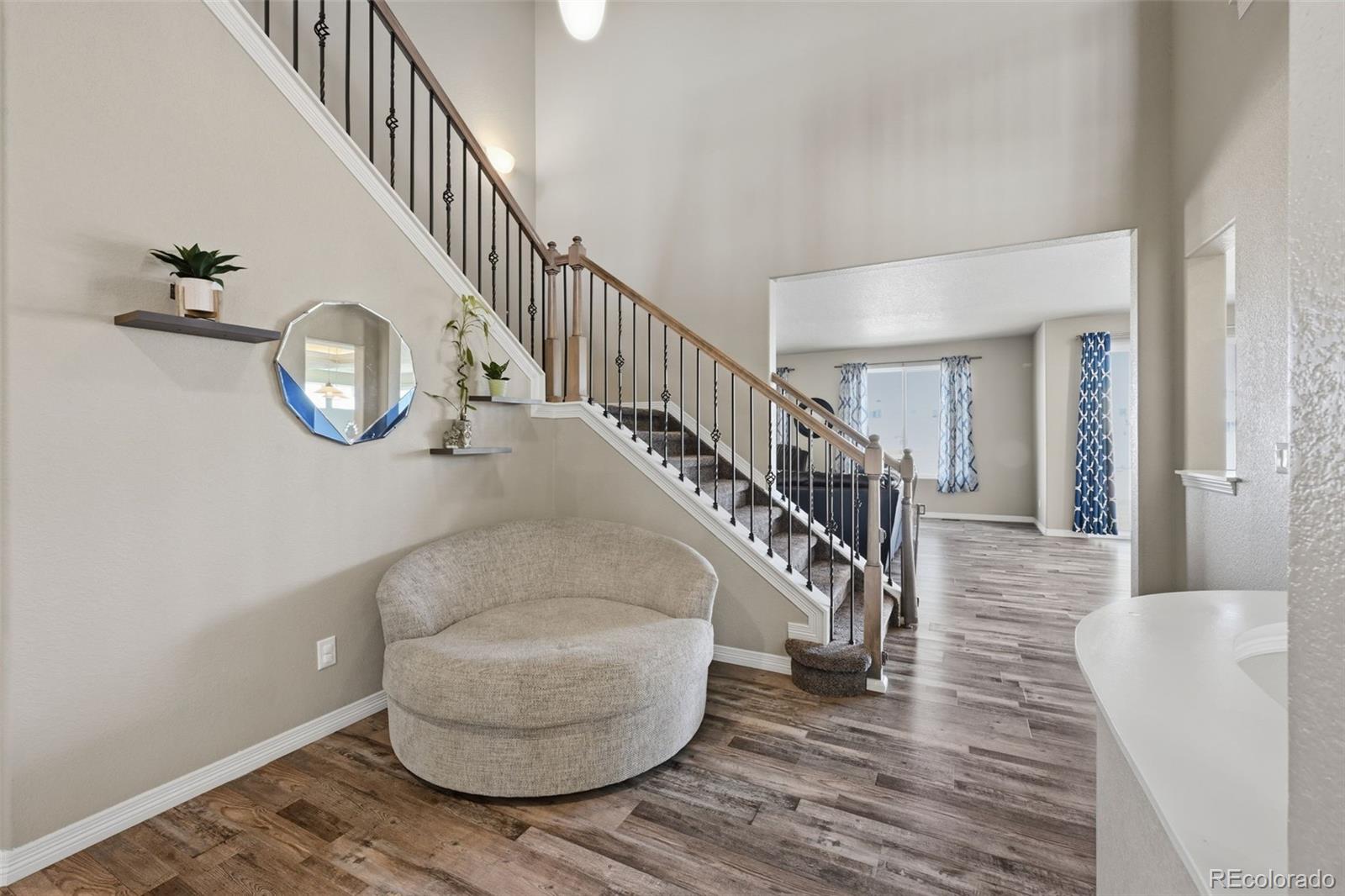 Entry foyer with a curved accent chair, floating shelves, and carpeted staircase with iron railing.