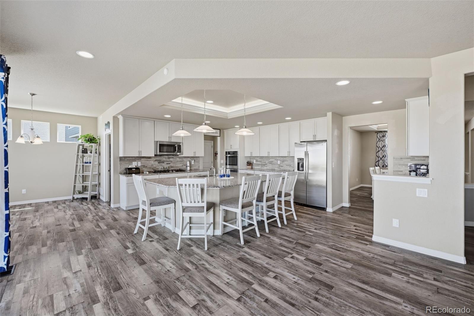 Open kitchen with a large island, white cabinets, stainless steel appliances, and wood-look flooring.