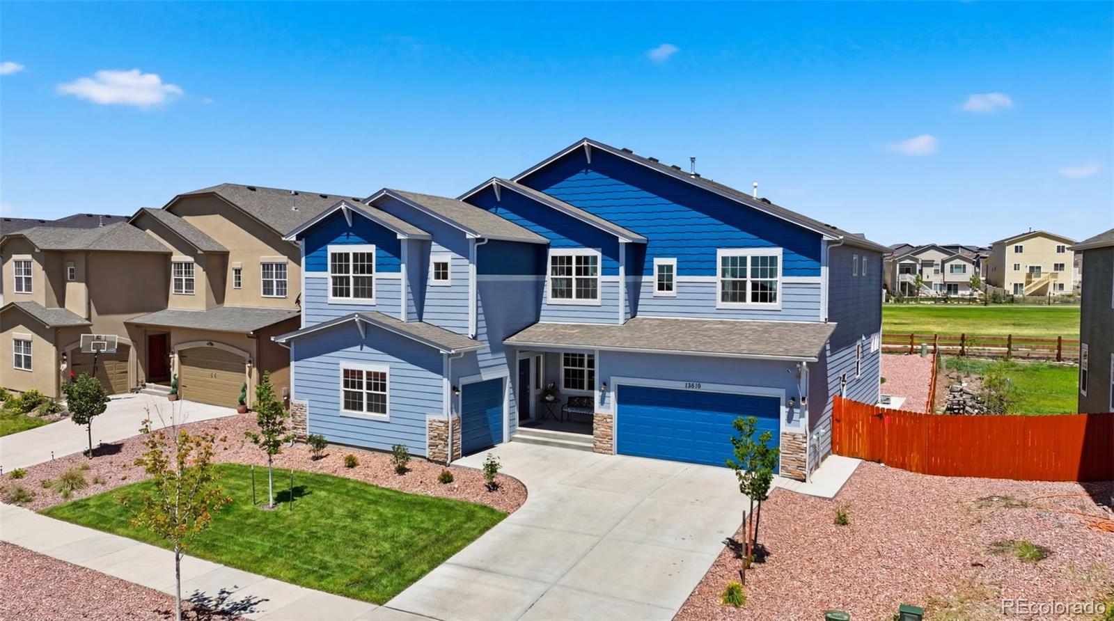 Blue two-story home with an attached garage, front lawn, and red side fence.