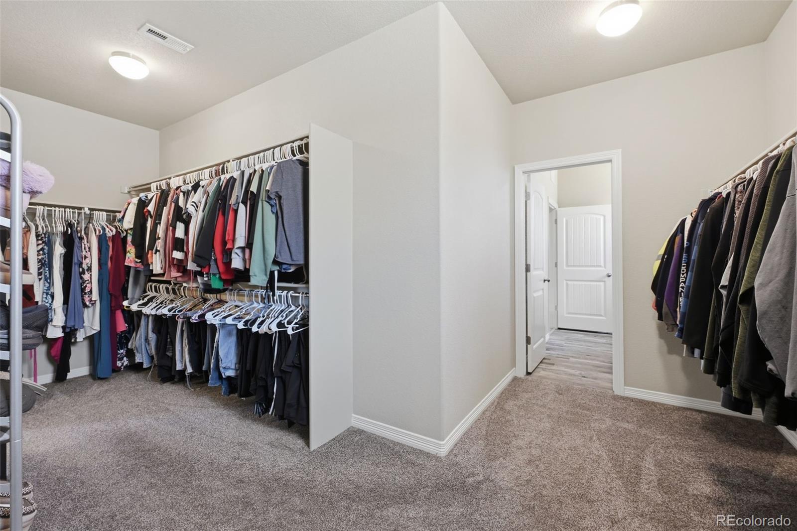 Walk-in closet with clothing on open racks and a doorway to the hall.