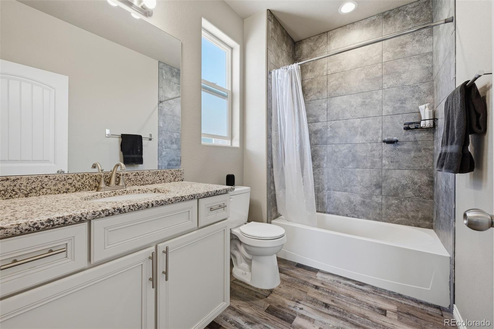 Bathroom with granite vanity, gray tile tub and shower, and a tall window.