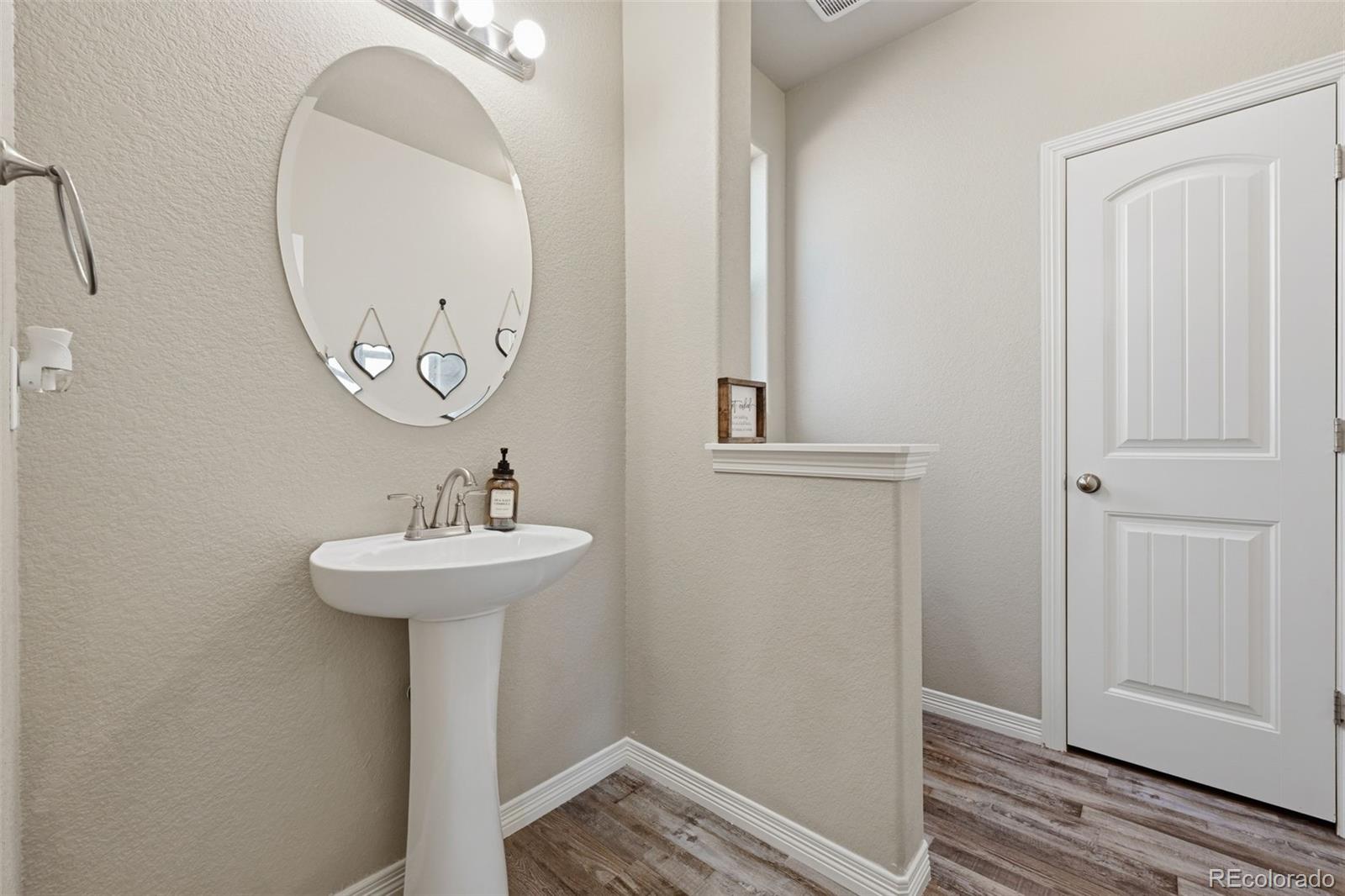 Half bathroom with a white pedestal sink, oval mirror, and wood-look flooring.