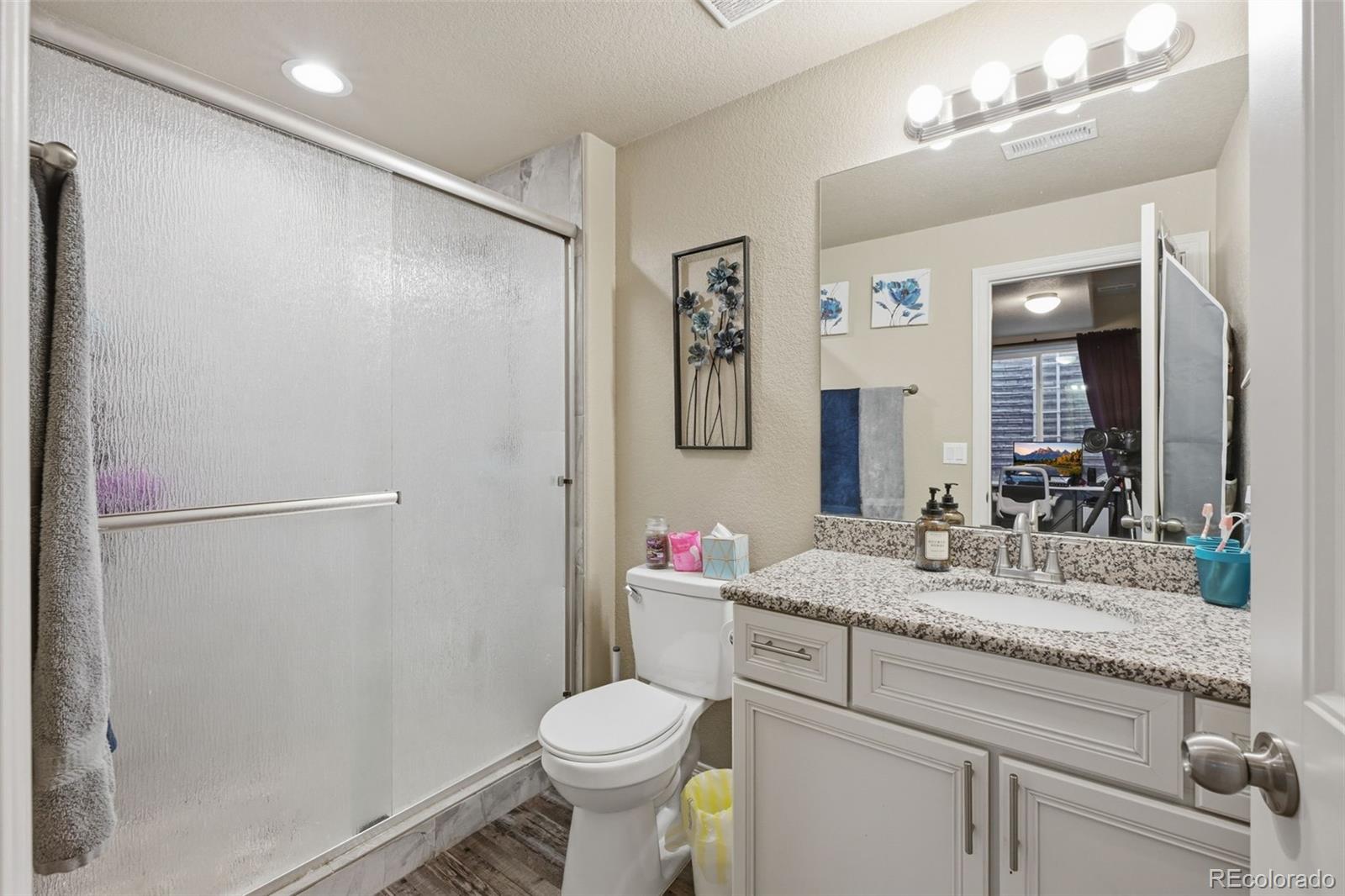 Bathroom with frosted-glass shower, white vanity, speckled granite countertop, and large mirror.